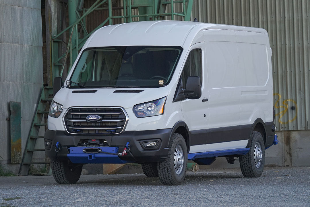 A white van parked in front of a green metal wall, featuring close-ups of its headlight, tire, door handle, and grille.