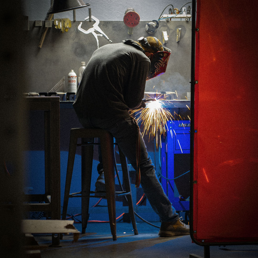 A man welding a piece of metal with visible sparks, captured in a close-up view.