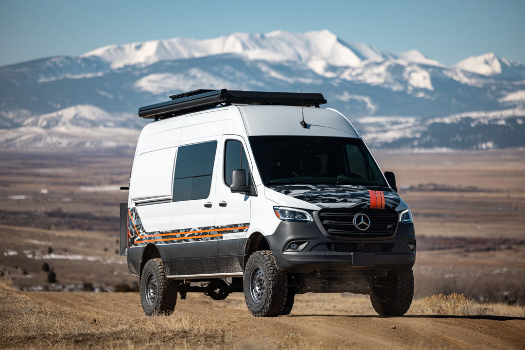 White van on a dirt road with mountains in the background, showcasing the Van Compass Striker AWD 2 Lift Kit for enhanced off-road capability and clearance.