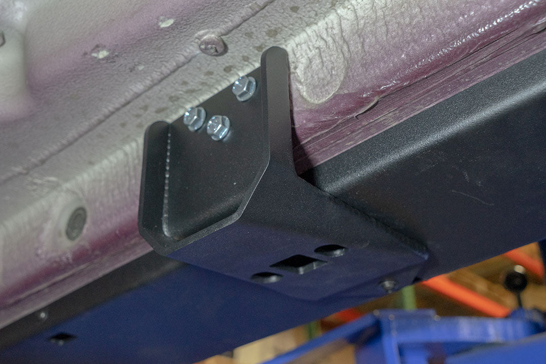 Rocker Guards - Sprinter 4x4 (2015-2022 170 Wheelbase) by Van Compass, showing a metal bracket with screws attached to a vehicle's chassis for enhanced protection and rigidity.