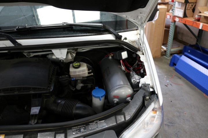 AIR SYSTEM MOUNT - SPRINTER (2007-2018) by VAN COMPASS installed under the hood, showing the bracket and a grey cylinder with red and white labels.