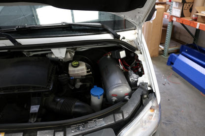 AIR SYSTEM MOUNT - SPRINTER (2007-2018) by VAN COMPASS installed under the hood, showing the bracket and a grey cylinder with red and white labels.