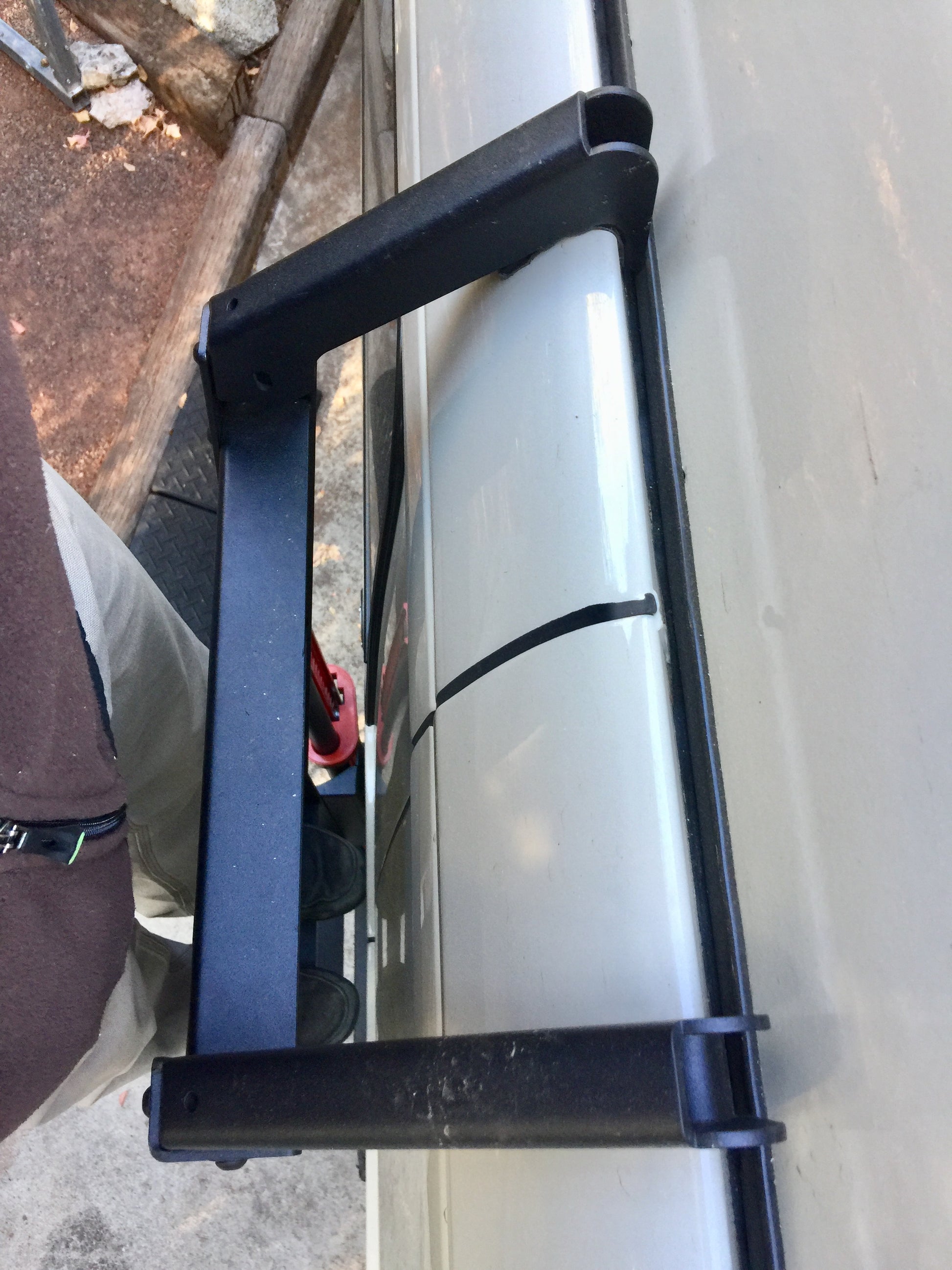 Side view of a black handle on a white van, part of the SIDE LADDER - SPRINTER (2007-CURRENT, LOW ROOF ONLY) by VAN COMPASS, attached to the roof ledge.