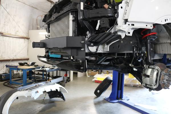 Front receiver hitch for Ford Transit (2013+ 1500, 2500, 3500) by Van Compass, displayed in a garage with visible bumper and black wheels.