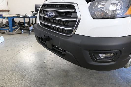 Front view of a white Ford Transit showcasing the Van Compass front receiver hitch for bike racks or winch cradle, compatible with front-end sensors.