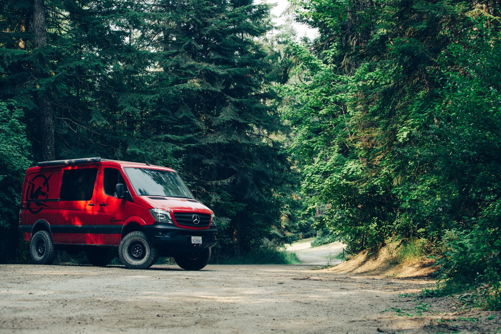 Red van equipped with the STRIKER 4X4 2 Lift Kit parked on dirt road, showcasing enhanced ground clearance and off-road capabilities.